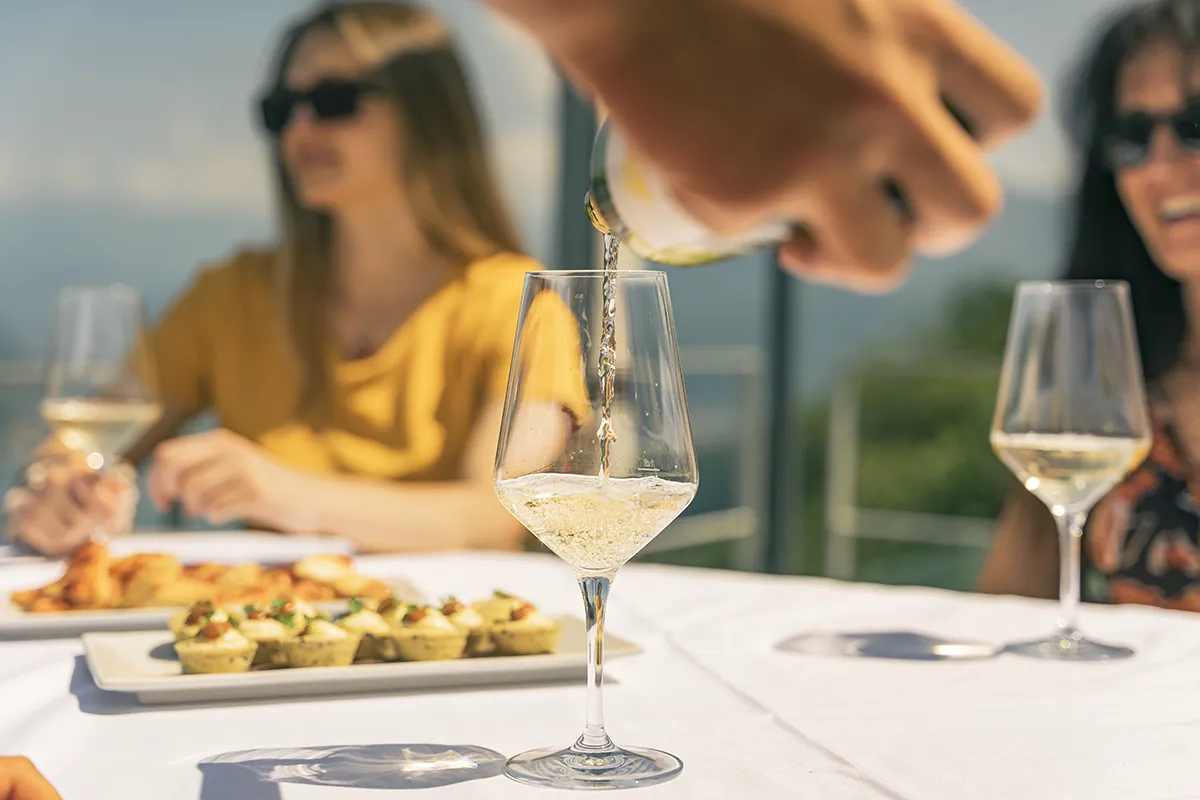 Sommelier versa vino bianco calice tavolo esterno lago Borgovecchio